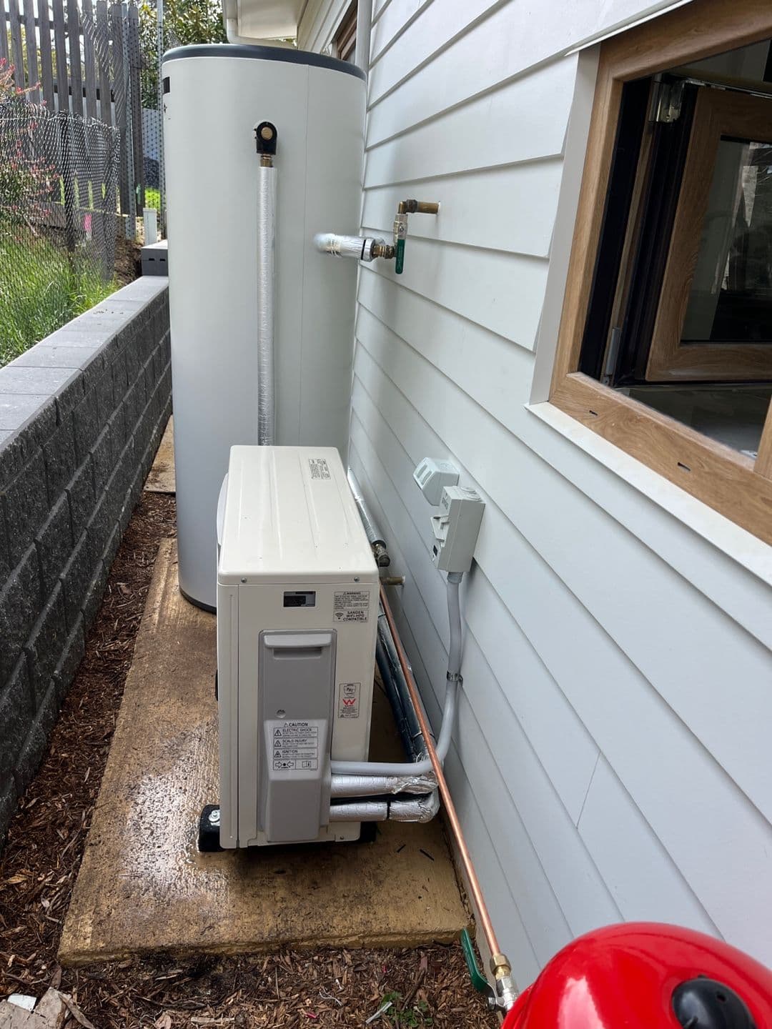 External Sanden heat pump hot water system installed in a narrow residential service area.