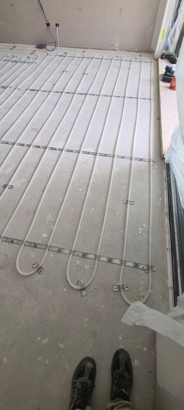 Close view of hydronic heating pipes secured to fixing rails before screed installation.