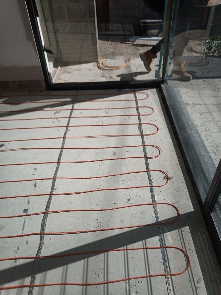 Electric in-screed underfloor heating cables installed beside sliding glass doors in a Lilyfield home.