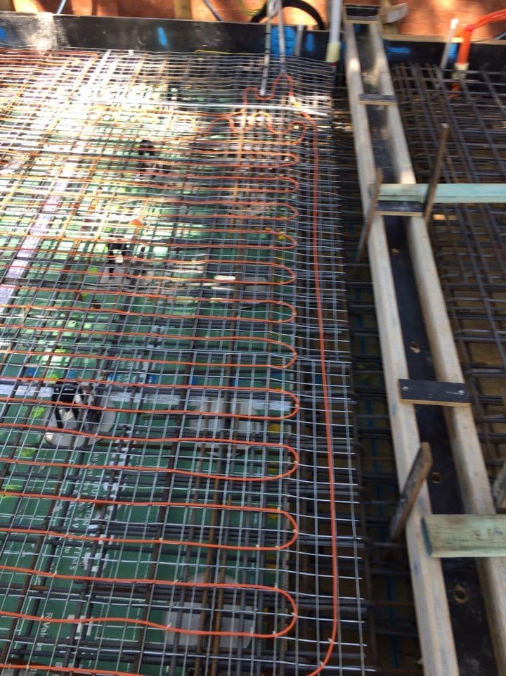 Electric underfloor heating cables coordinated around slab penetrations and structural formwork.