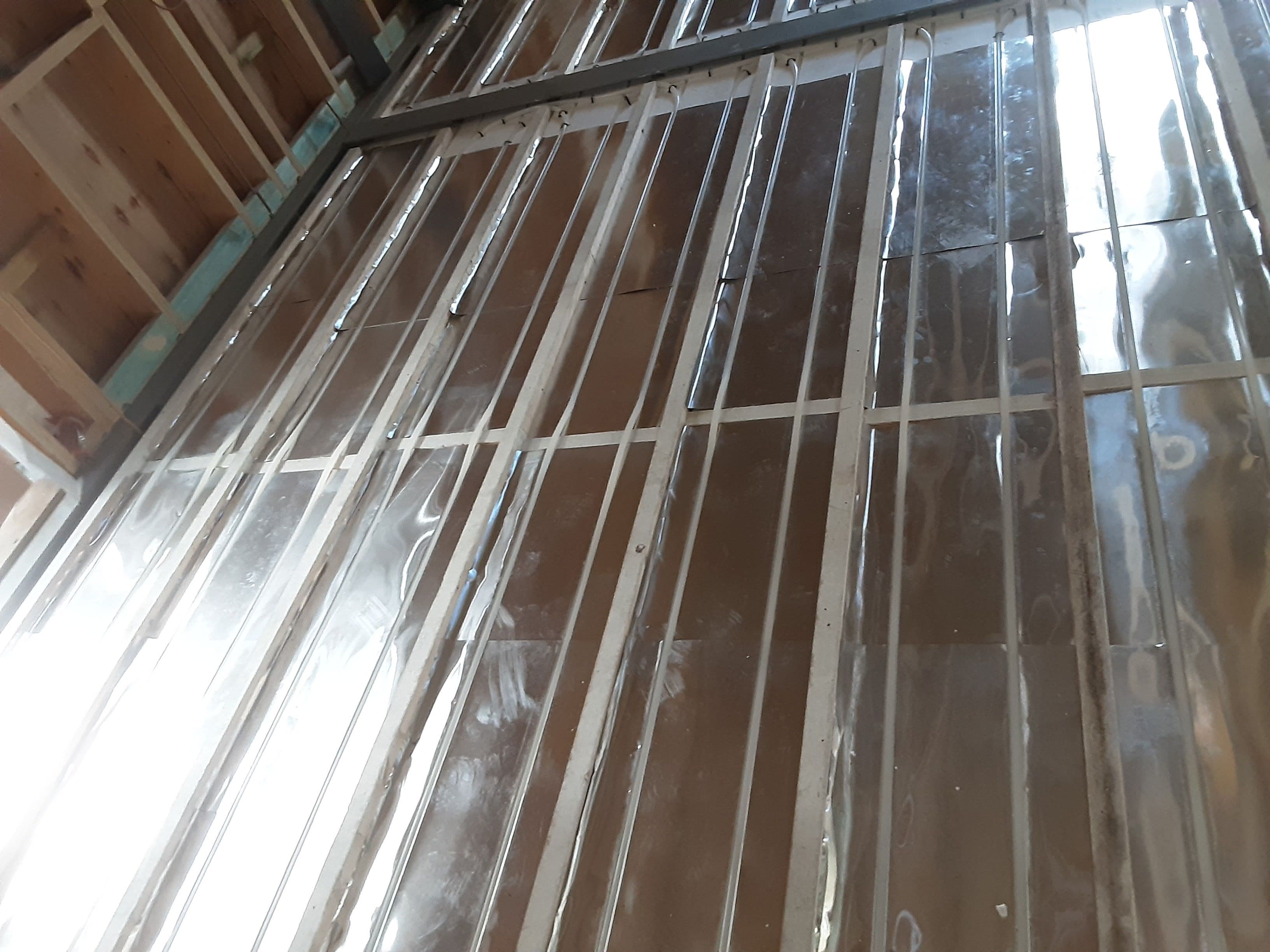 Between-battens hydronic pipework laid over insulation and reflective heat-transfer plates.