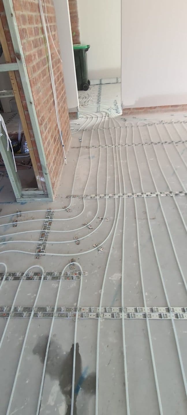 Evenly spaced 10mm hydronic heating pipes installed beside a glazed exterior wall.